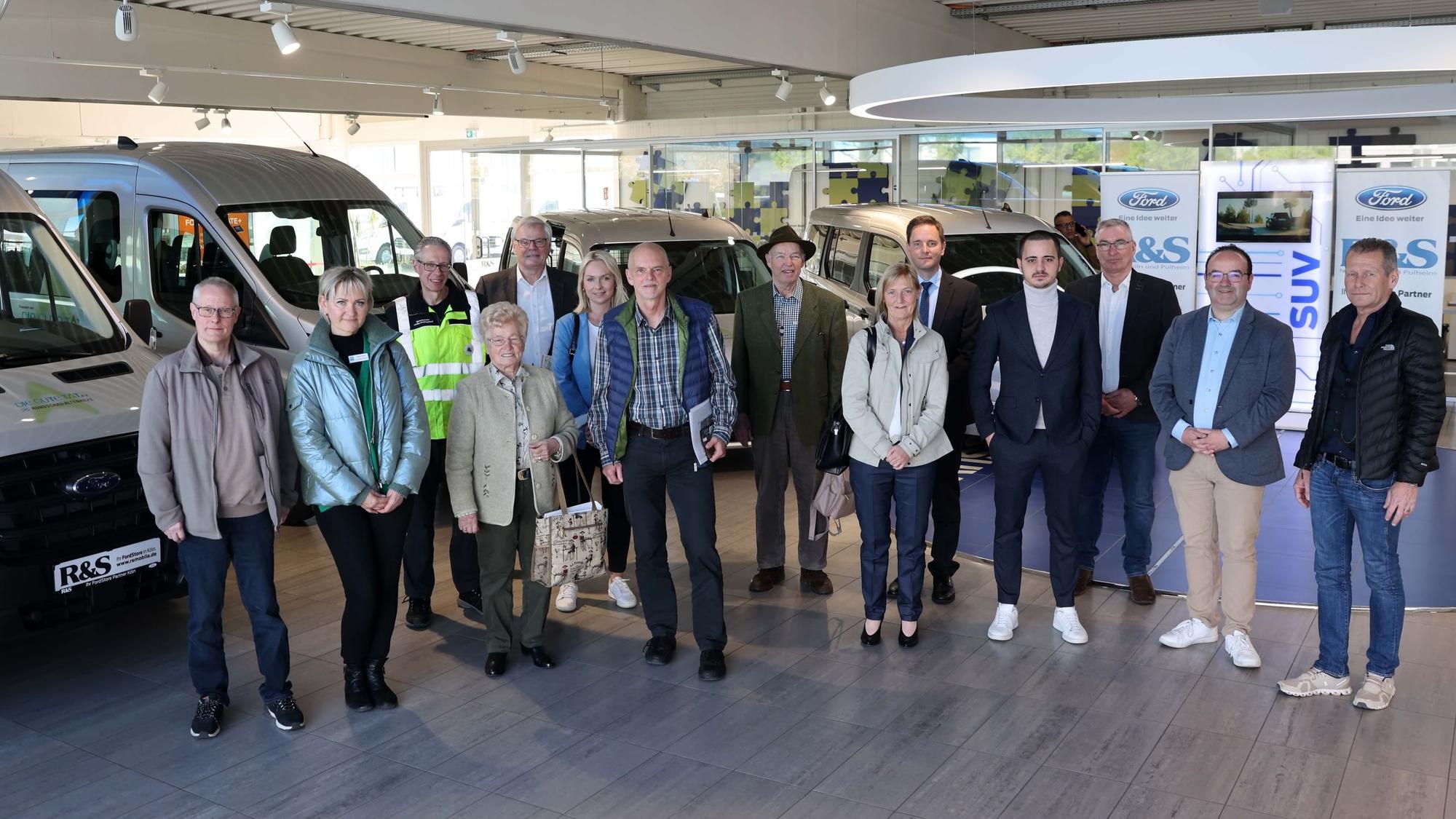 Mehrere Personen stehen in einem Autohaus vor Autos.