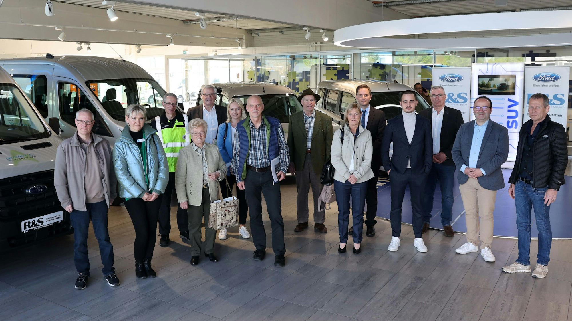 Mehrere Personen stehen in einem Autohaus vor Autos.