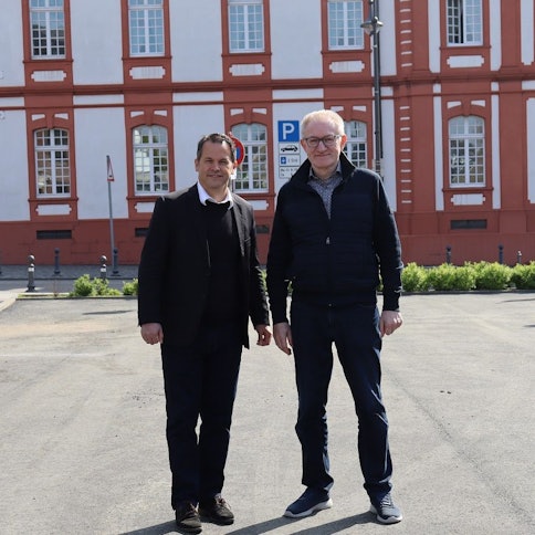 Die beiden Männer tragen dunkle Klamotten, stehen nebeneinander und blicken in die Kamera.