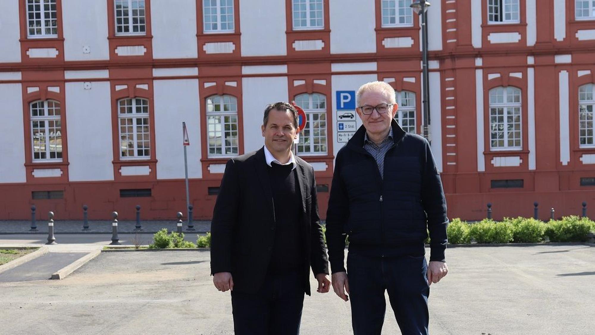 Die beiden Männer tragen dunkle Klamotten, stehen nebeneinander und blicken in die Kamera.