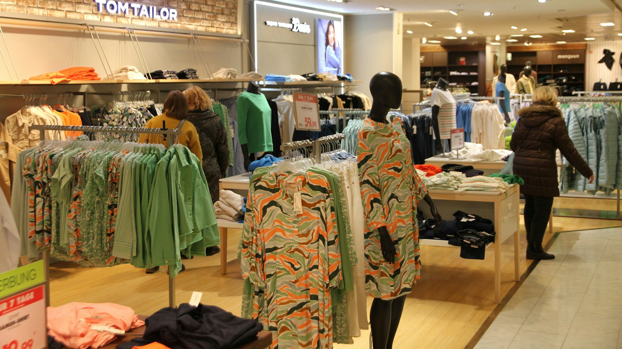 Auf Kleiderständern hängen Kleider und Blusen, im Hintergrund ist eine Kundin.