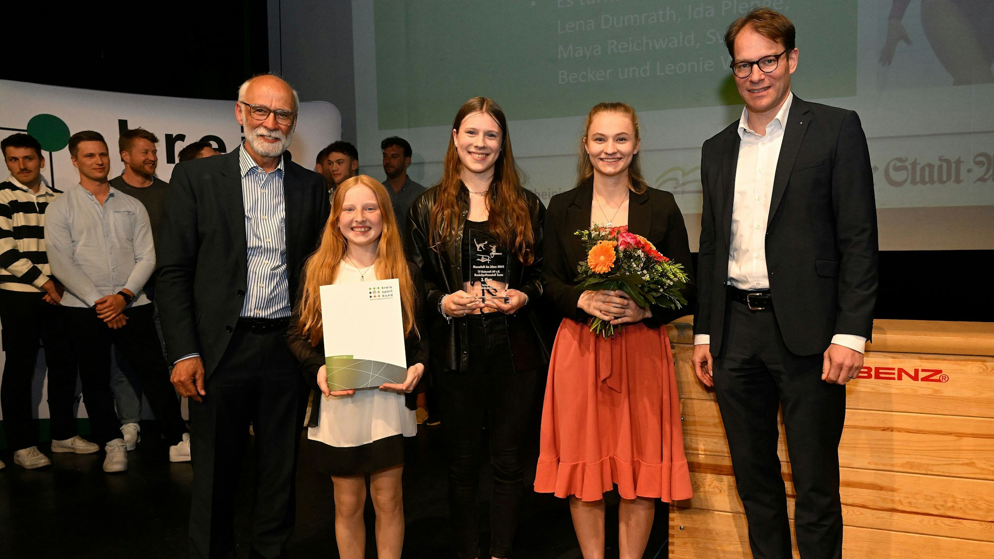 Die Kunstturnerinnen des TV Herkenrath stehen mit Kreissportbund-Chef Uli Heimann (l.) und den Regionalvorstand der Kreisparkasse Köln, Gunter Derksen, auf einer Bühne.