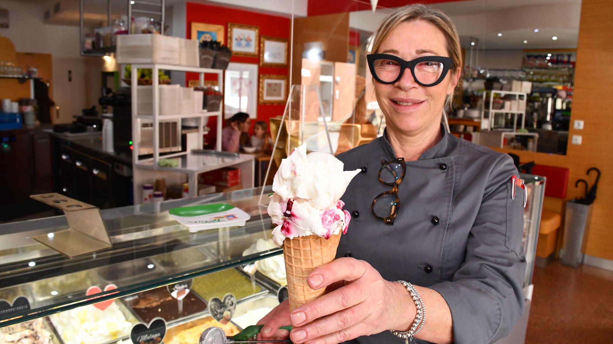 Eine Frau steht mit einem Eis in Hand vor der Eistheke im Innenraum des Eiscafés.