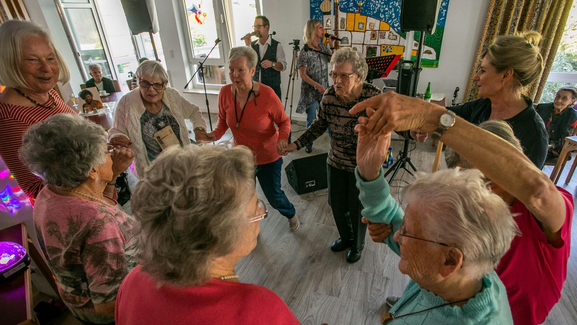 Senioren und Seniorinnen tanzen zu Schlagermusik in einem Partyraum.