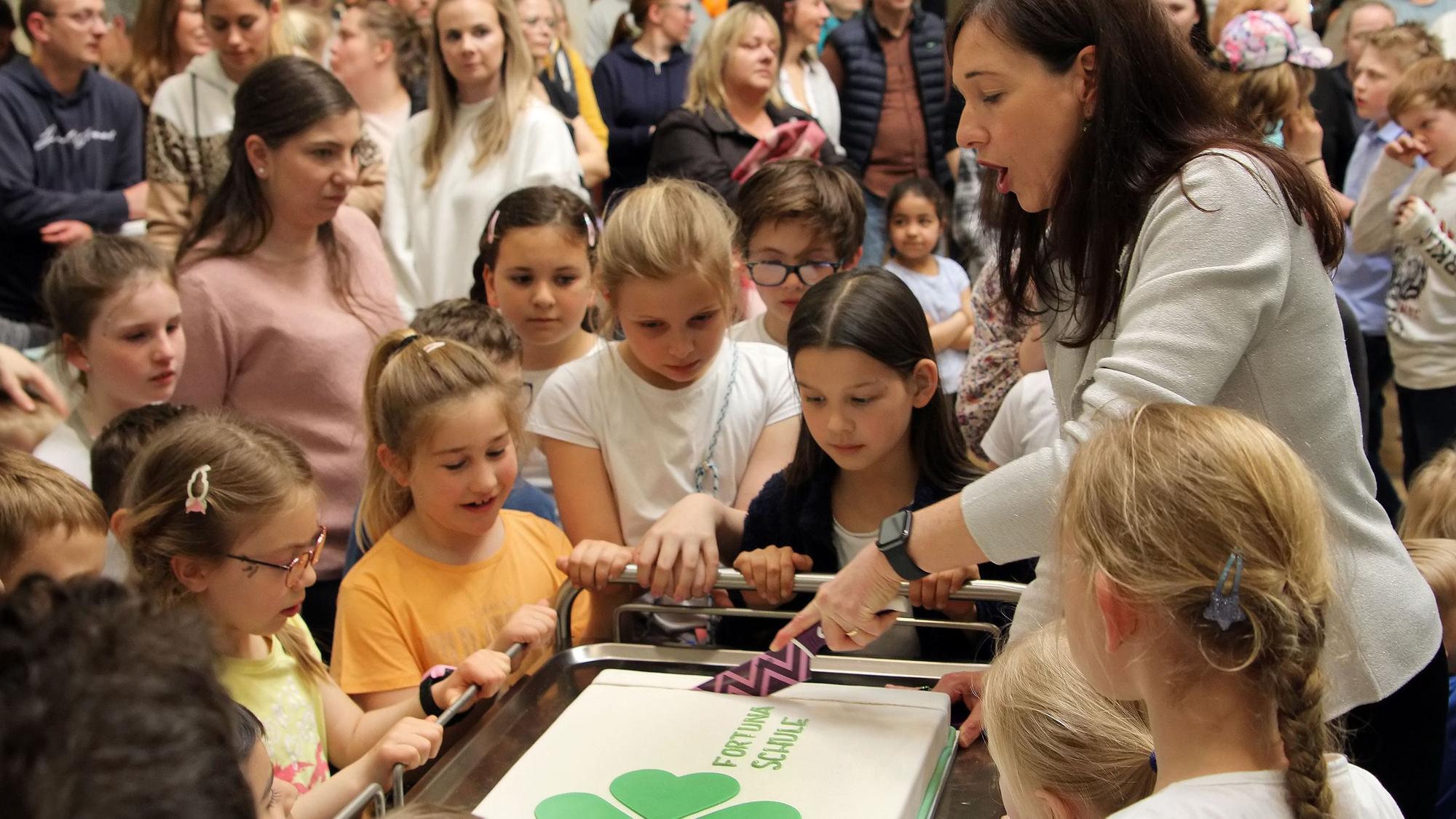 Von Kindern umringt schnitt Rektorin Britta Bockschewsky bei der Eröffnungsfeier der Oberaußemer Fortunaschule eine mit dem Kleeblatt-Logo verzierte Torte an.