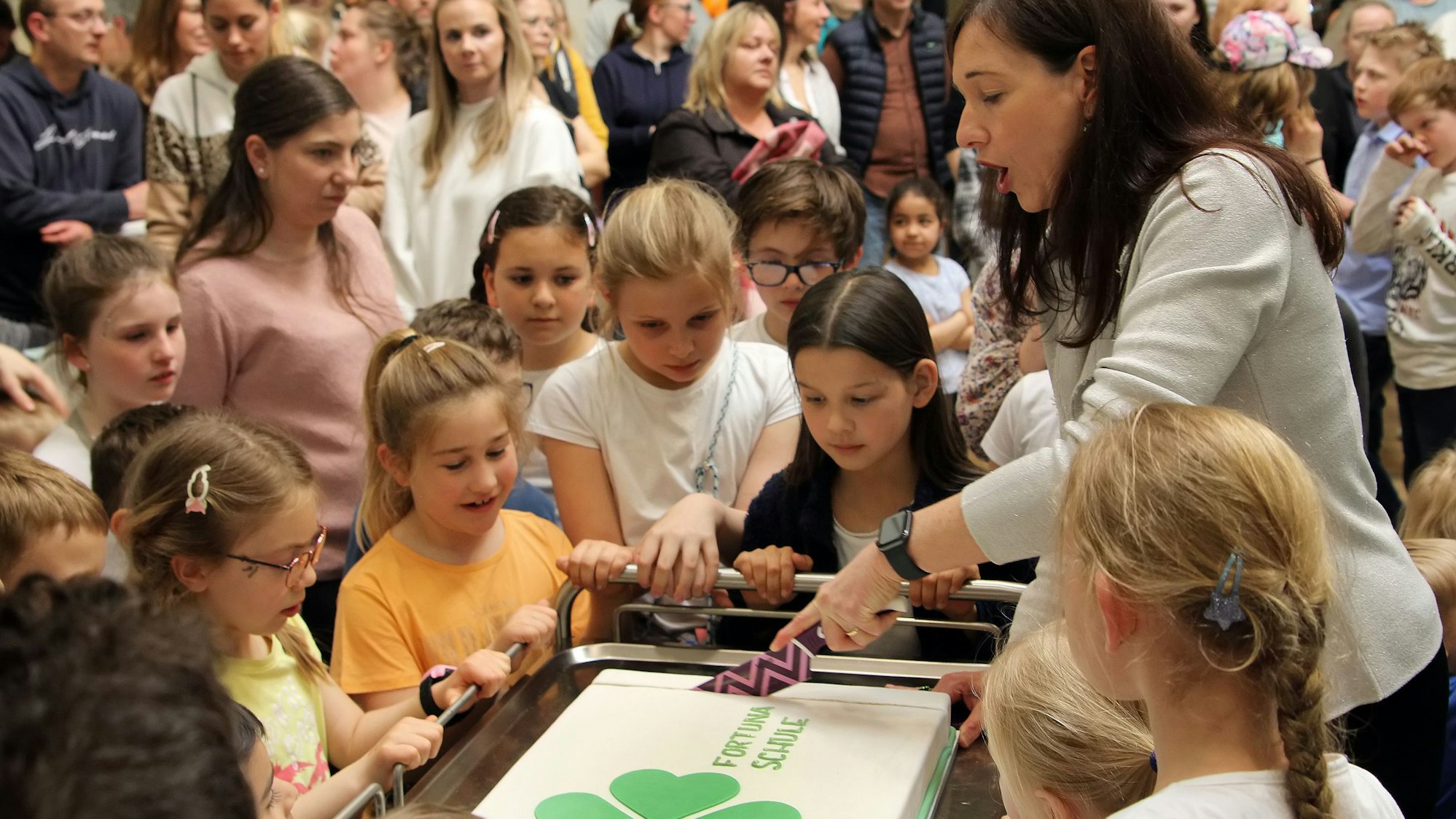 Von Kindern umringt schnitt Rektorin Britta Bockschewsky bei der Eröffnungsfeier der Oberaußemer Fortunaschule eine mit dem Kleeblatt-Logo verzierte Torte an.