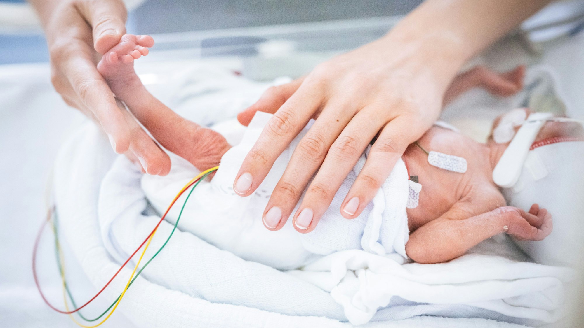 Mutter hält ihr Frühgeborenes im Inkubator fest.