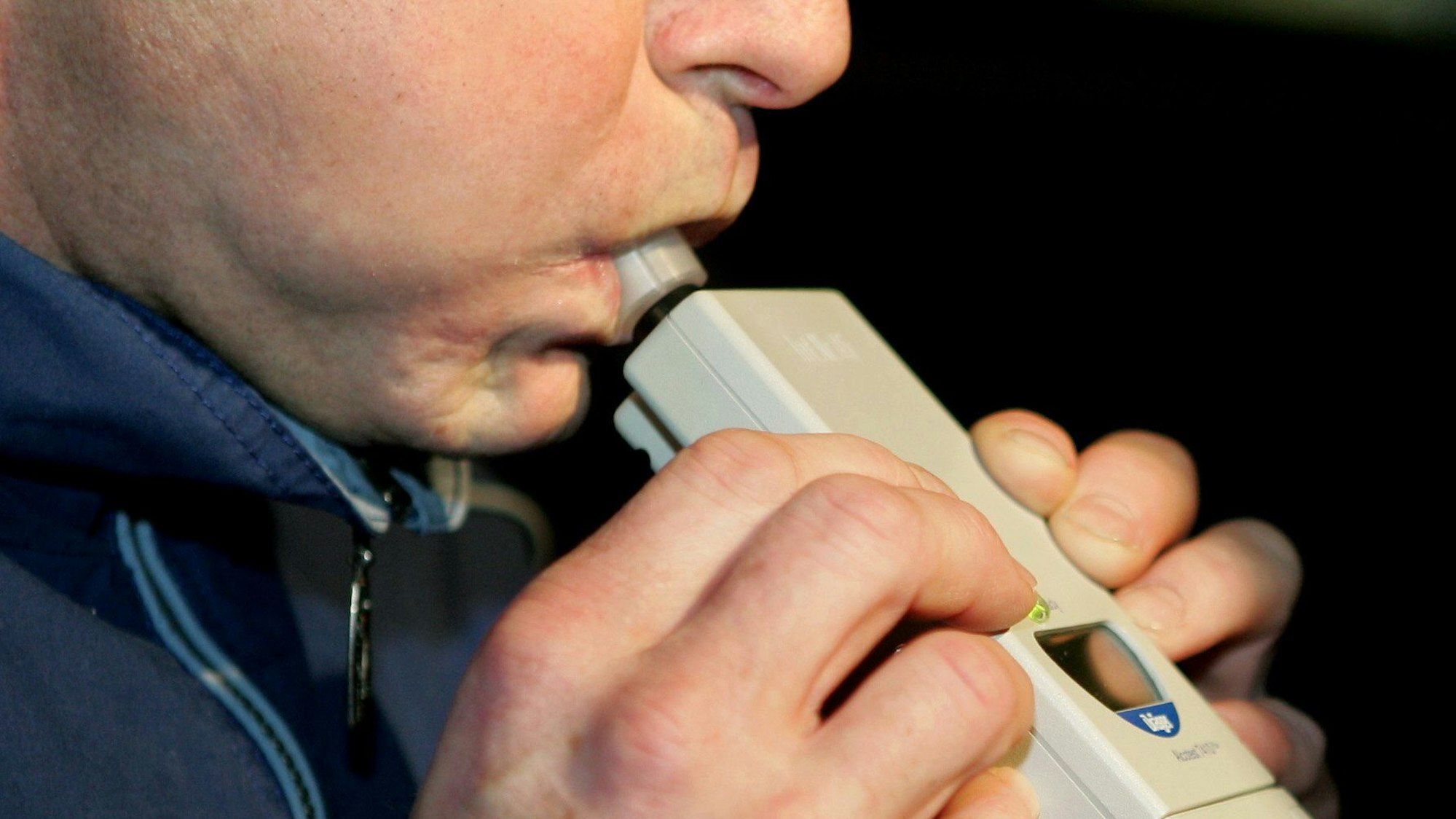 Das Bild zeigt, wie eine Person in ein Alkoholtestgerät pustet.
