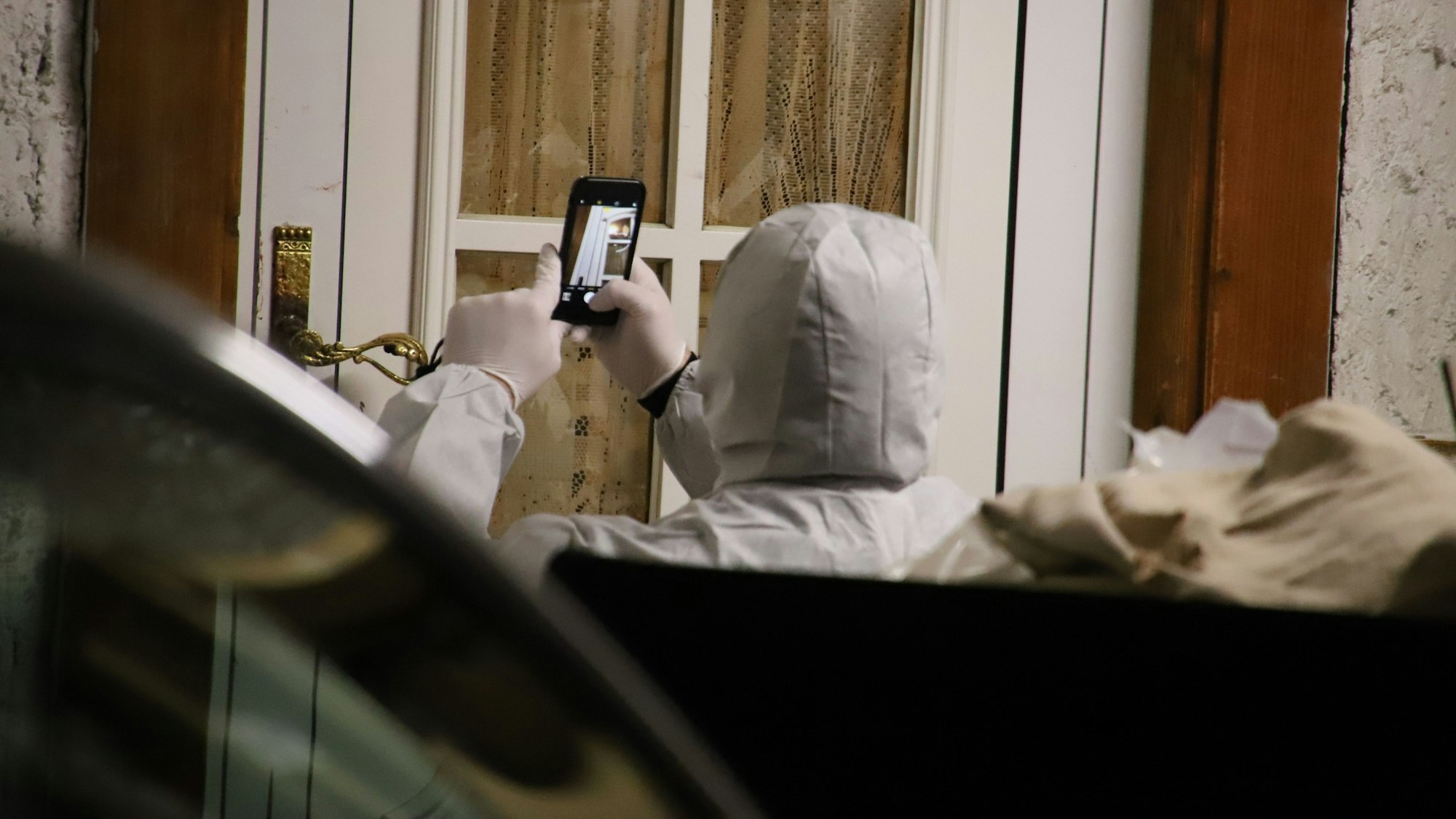 Eine Person im Schutzanzug fotografiert eine Fensterscheibe.