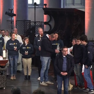 Diözesanjugendseelsorger Tobias Schwaderlapp steht am Altar des Altenberger Doms, während Frank Haag und Niklas Habers das Altenberger Licht für einen Hilfskonvoi ins ukrainische Butscha in Empfang nehmen.