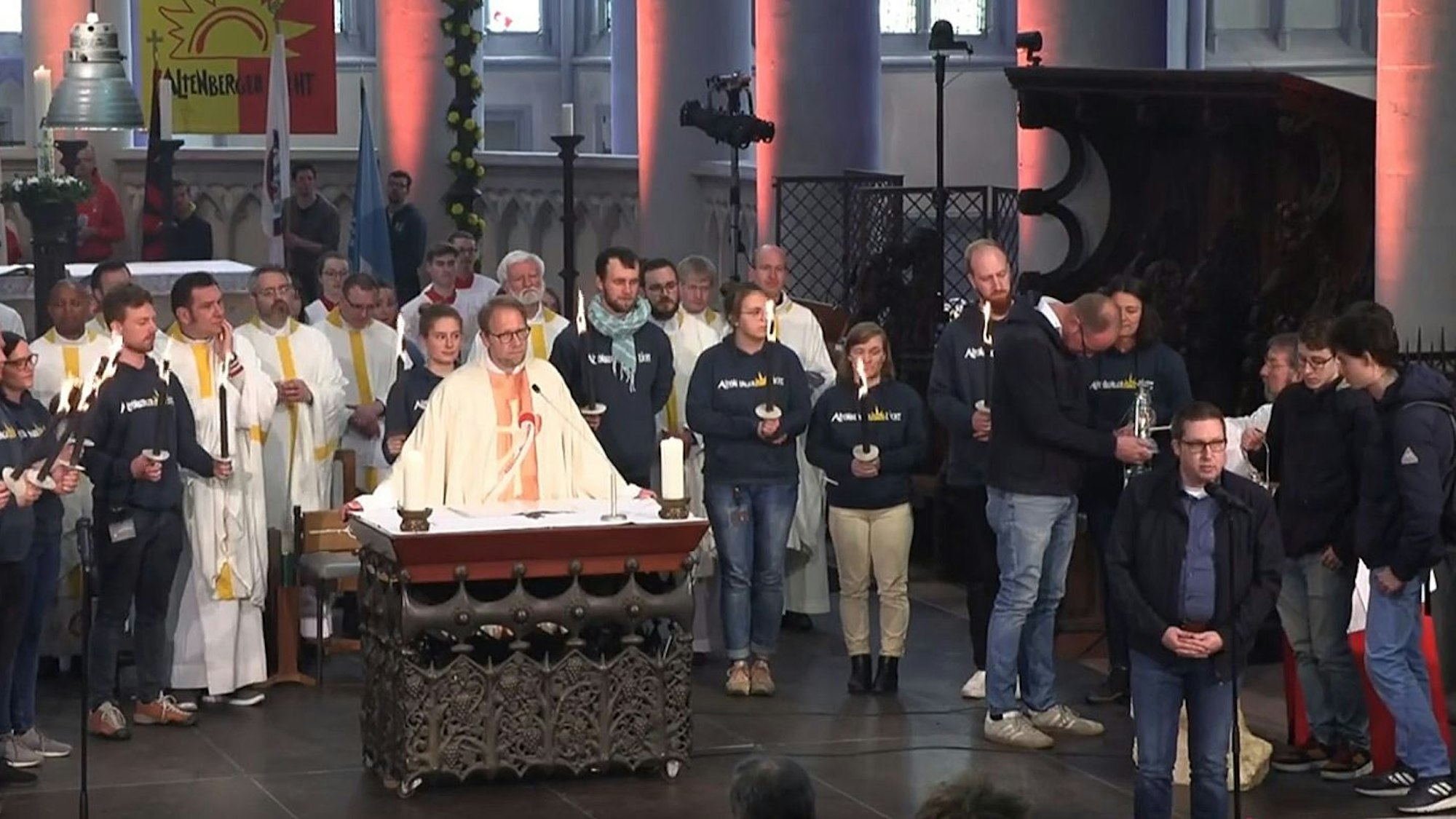 Diözesanjugendseelsorger Tobias Schwaderlapp steht am Altar des Altenberger Doms, während Frank Haag und Niklas Habers das Altenberger Licht für einen Hilfskonvoi ins ukrainische Butscha in Empfang nehmen.