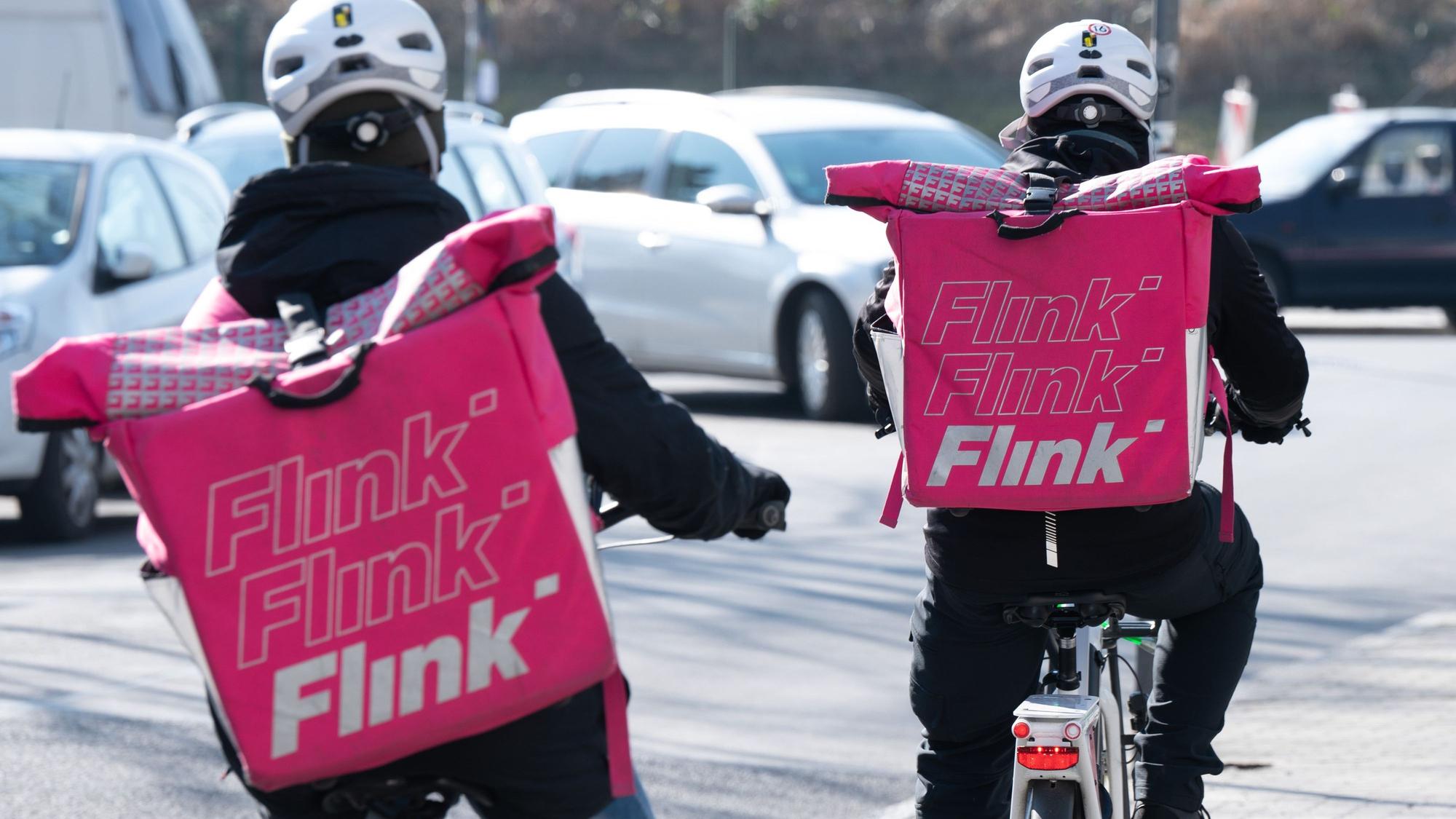 Zwei Fahrradkuriere des Lebensmittel-Lieferdienstes Flink tragen die markanten pinken Taschen des Unternehmens auf ihrem Rücken.