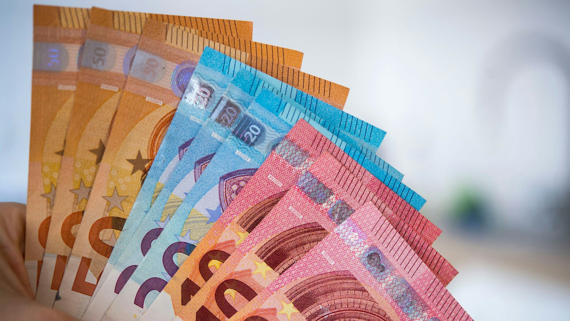 Eine Frau hält Banknoten von 10, 20 und 50 Euro gefächert in der Hand.