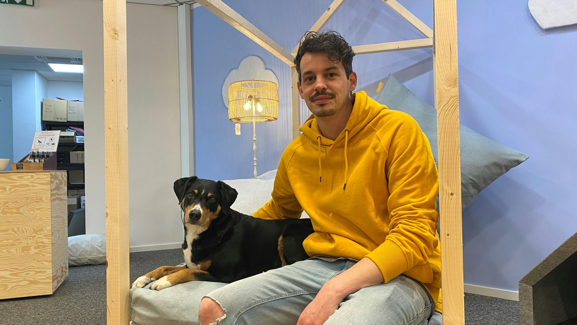 Es sind Manuel Mohlberg und seine Hündin Momo zu sehen. Er sitzt, die Hündin liegt.