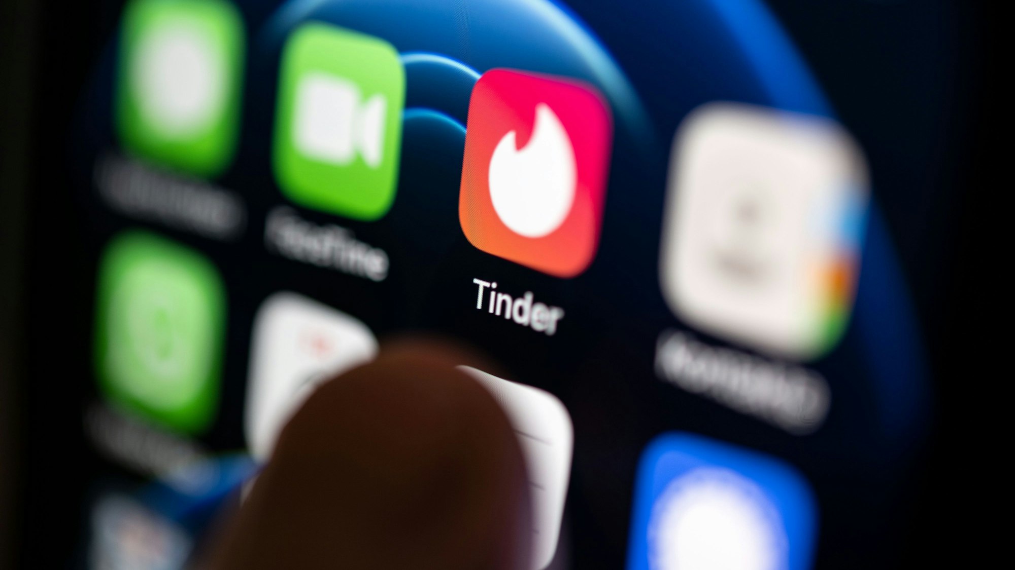 Ein Finger bedient ein Smartphone auf dem unter anderen die App von Tinder installiert ist.