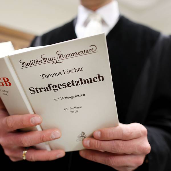Ein Richter im Gerichtssaal hält das Strafgesetzbuch (StGB) in der Hand.