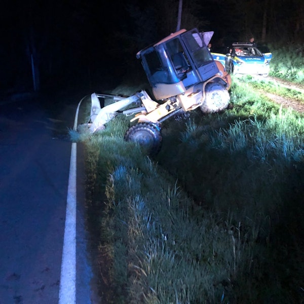 Ein Radlader liegt im Straßengraben und wird angeleuchtet, daneben steht ein Polizeiauto.