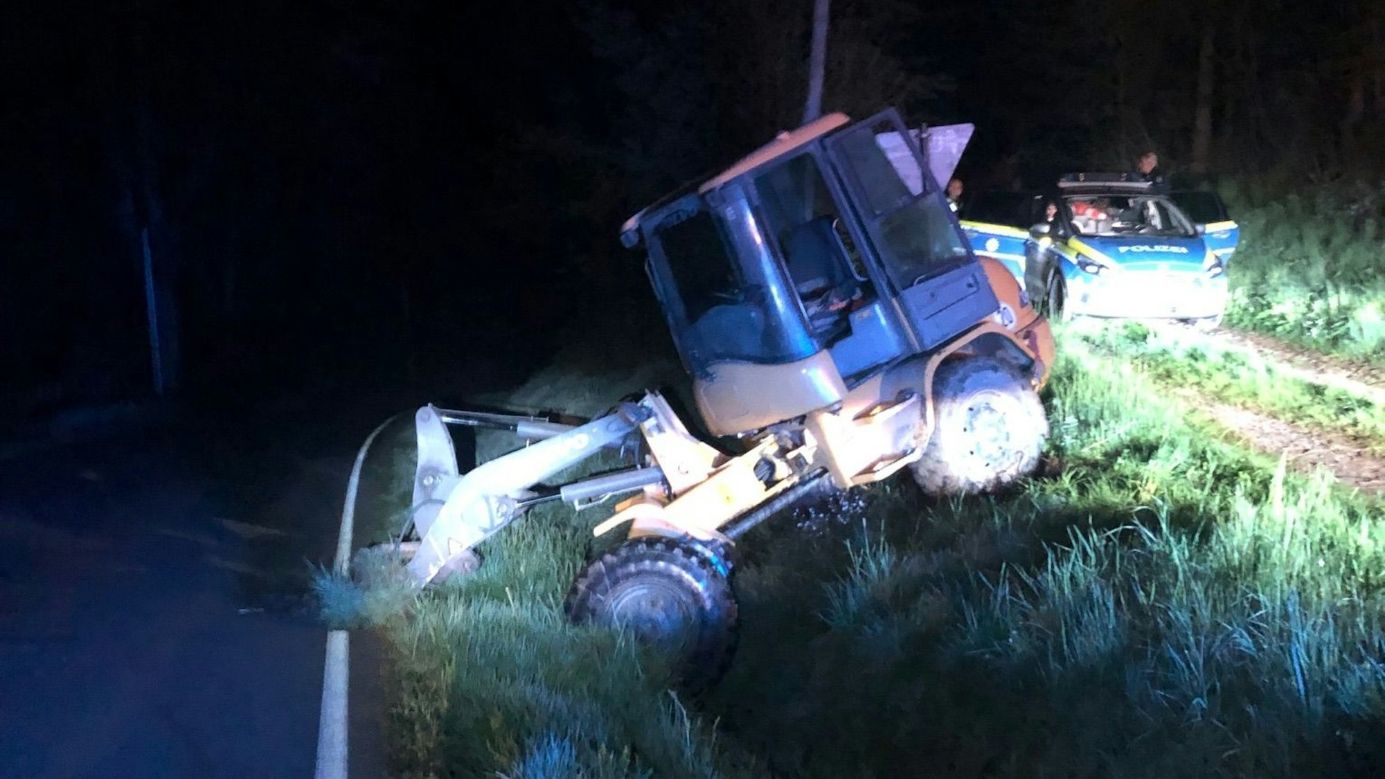 Ein Radlader liegt im Straßengraben und wird angeleuchtet, daneben steht ein Polizeiauto.