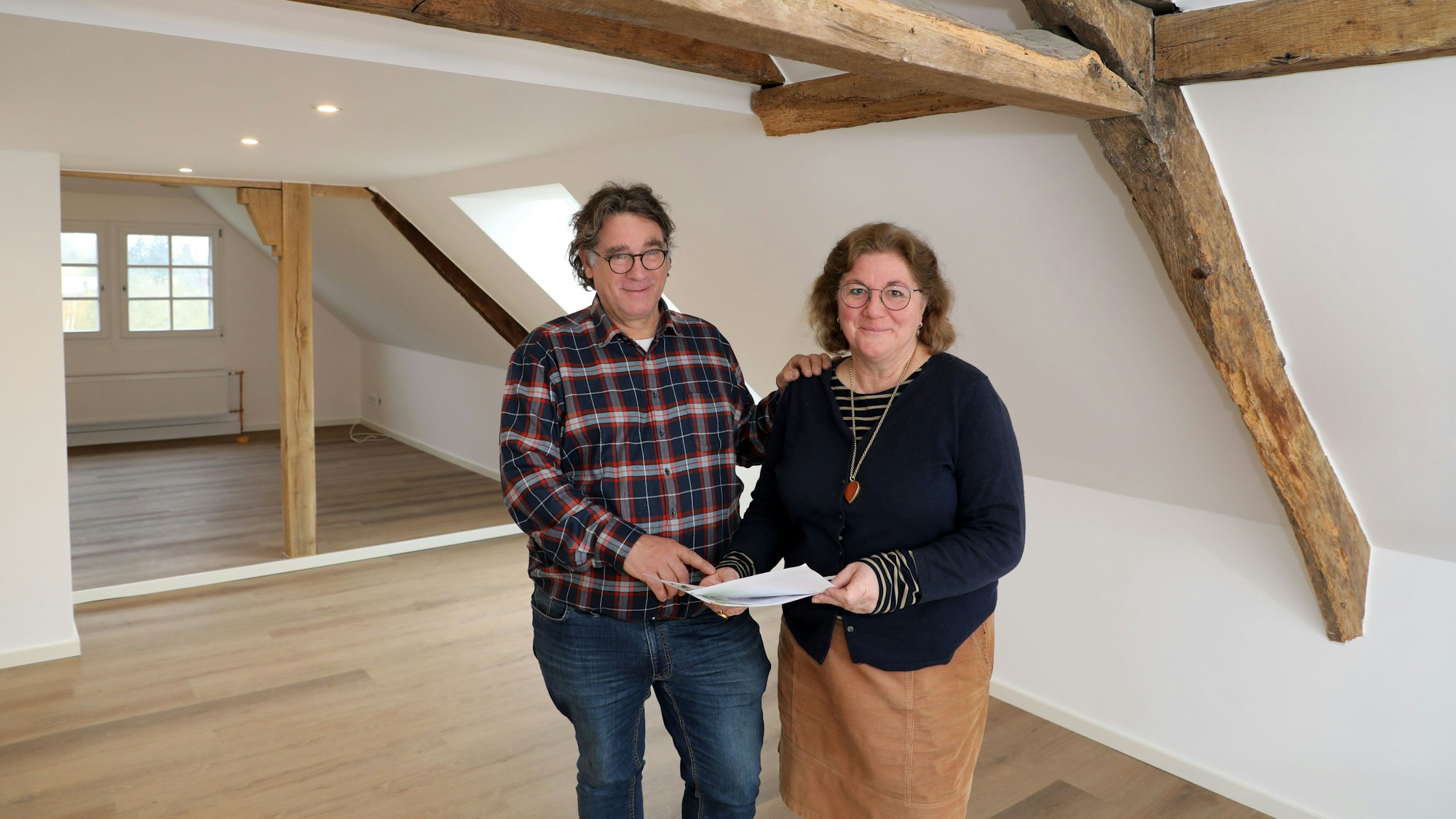 Anja Senff und Friedrich Bock stehen im Dachgeschoss des kernsanierten Gutshauses. Sie halten einige Zettel in der Hand.