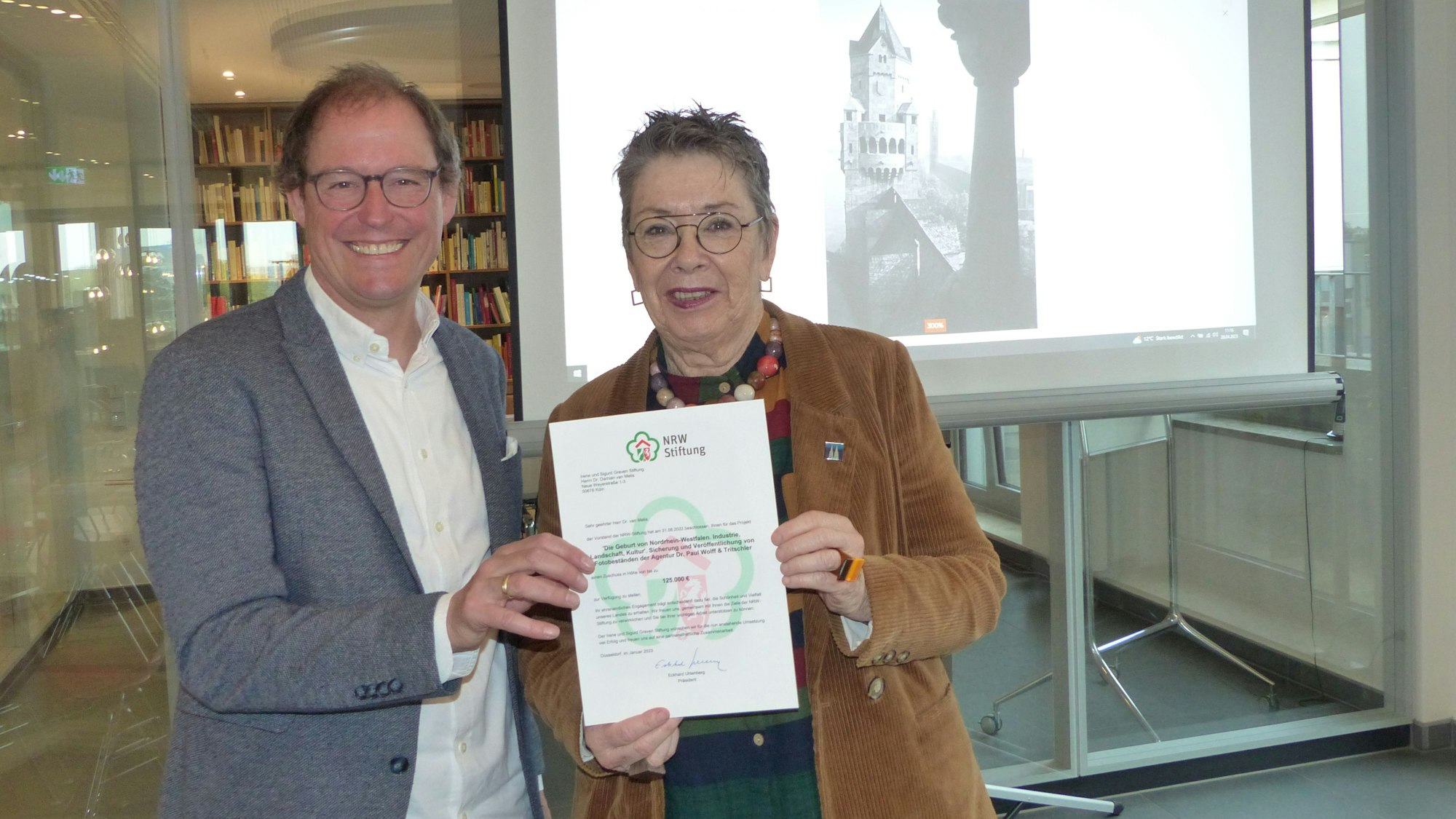 Damian van Melis und Barbara Schock-Werner halten eine Urkunde in die Kamera.