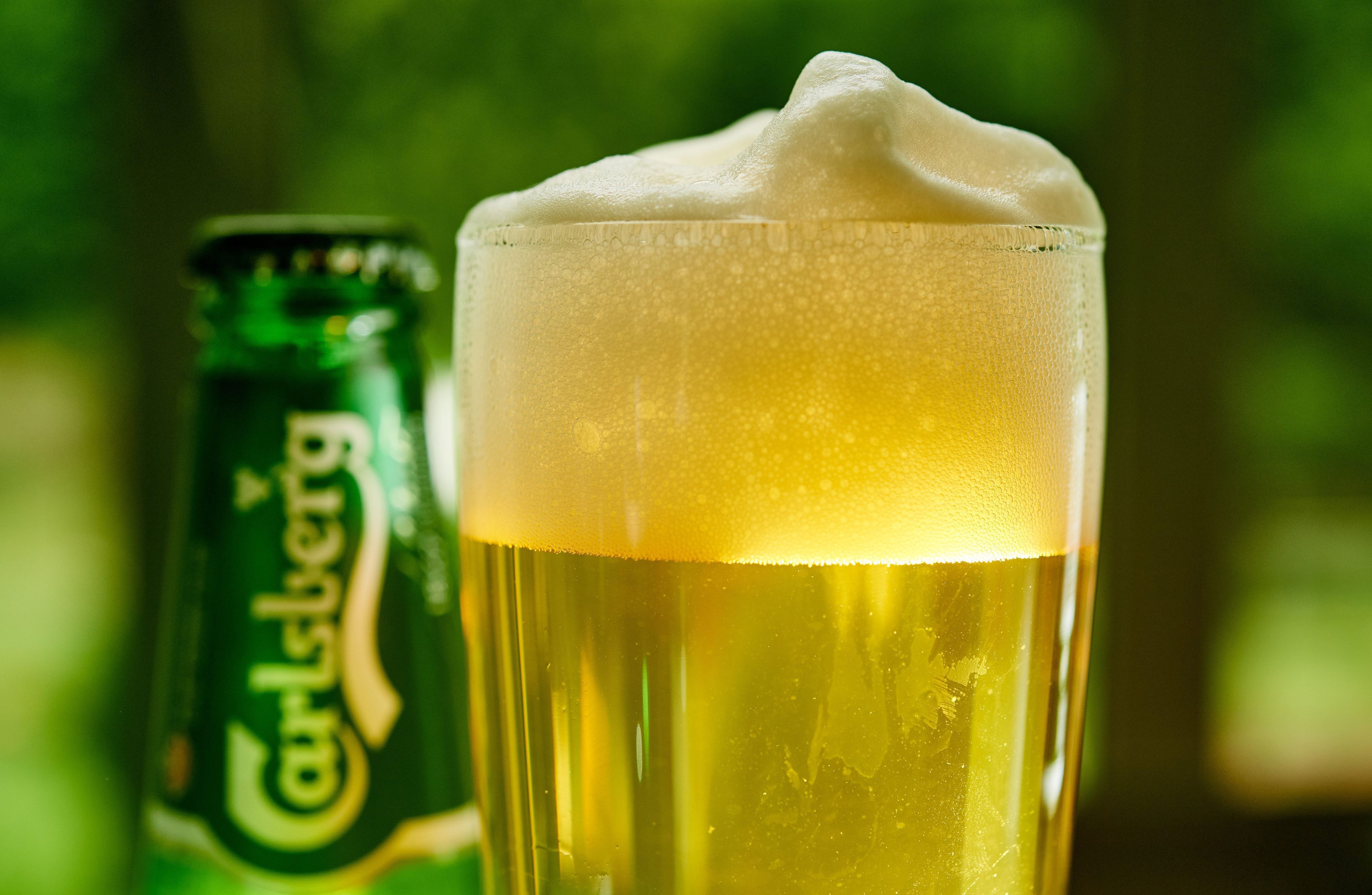 Ein Glas Bier und eine Bierflasche der Marke Carlsberg stehen auf einem Tisch.