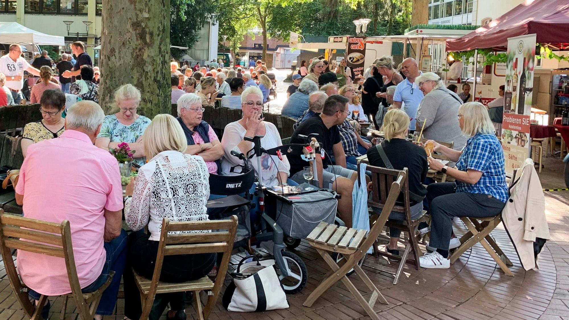 Menschen sitzen an Tischen auf einem Platz.
