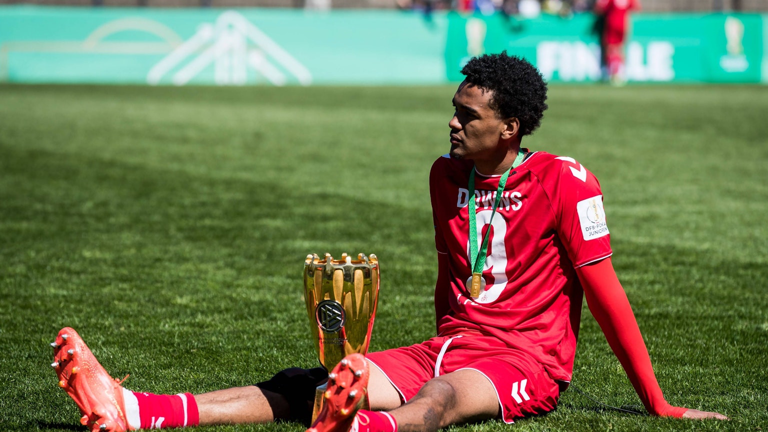 Damion Downs sitzt mit dem Pokal auf dem Rasen