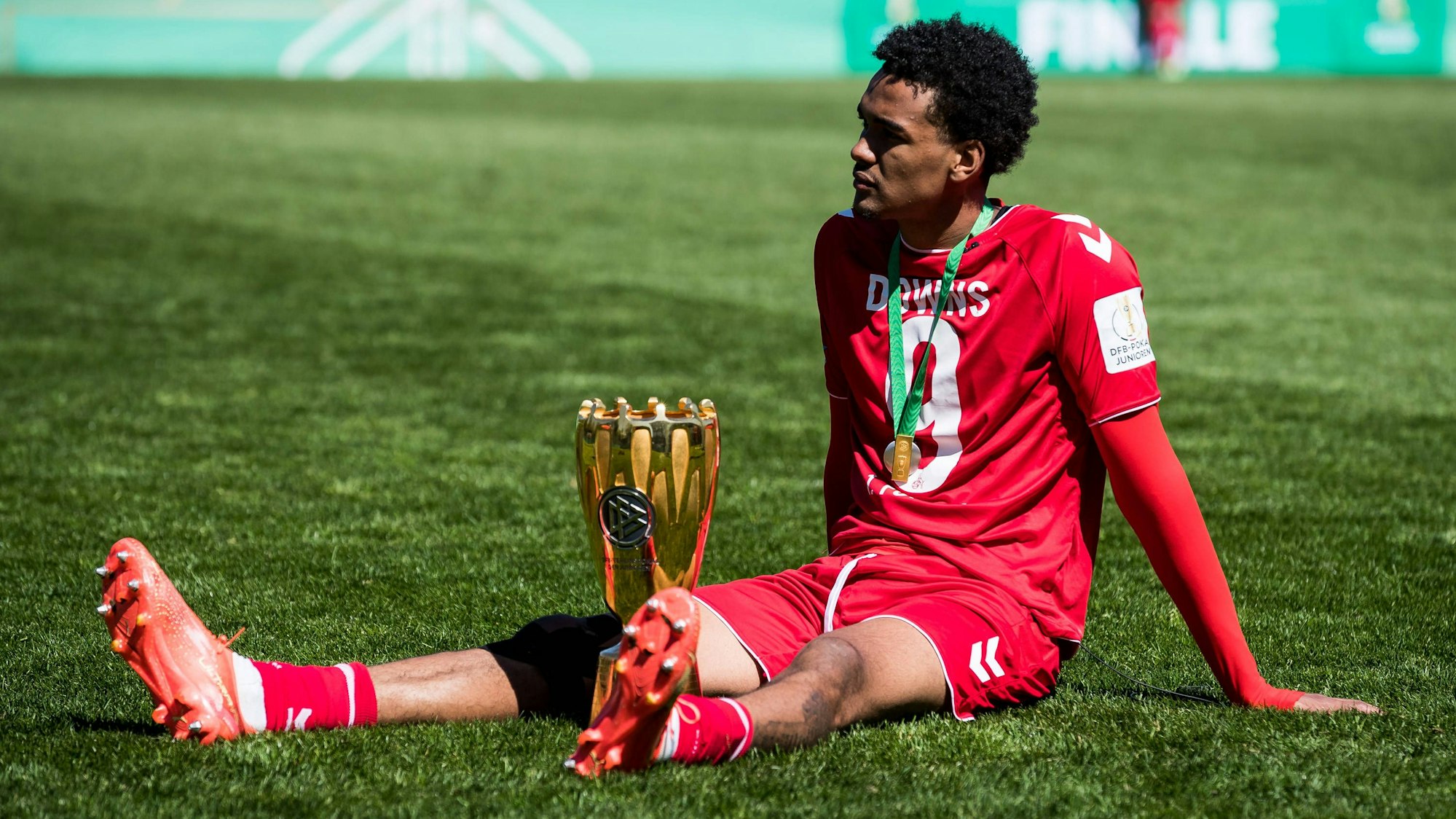 Damion Downs sitzt mit dem Pokal auf dem Rasen