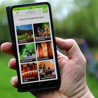 Die Freizeit-App von „Das Bergische“ wird auf einem Smartphone in einer Menschenhand dargestellt.