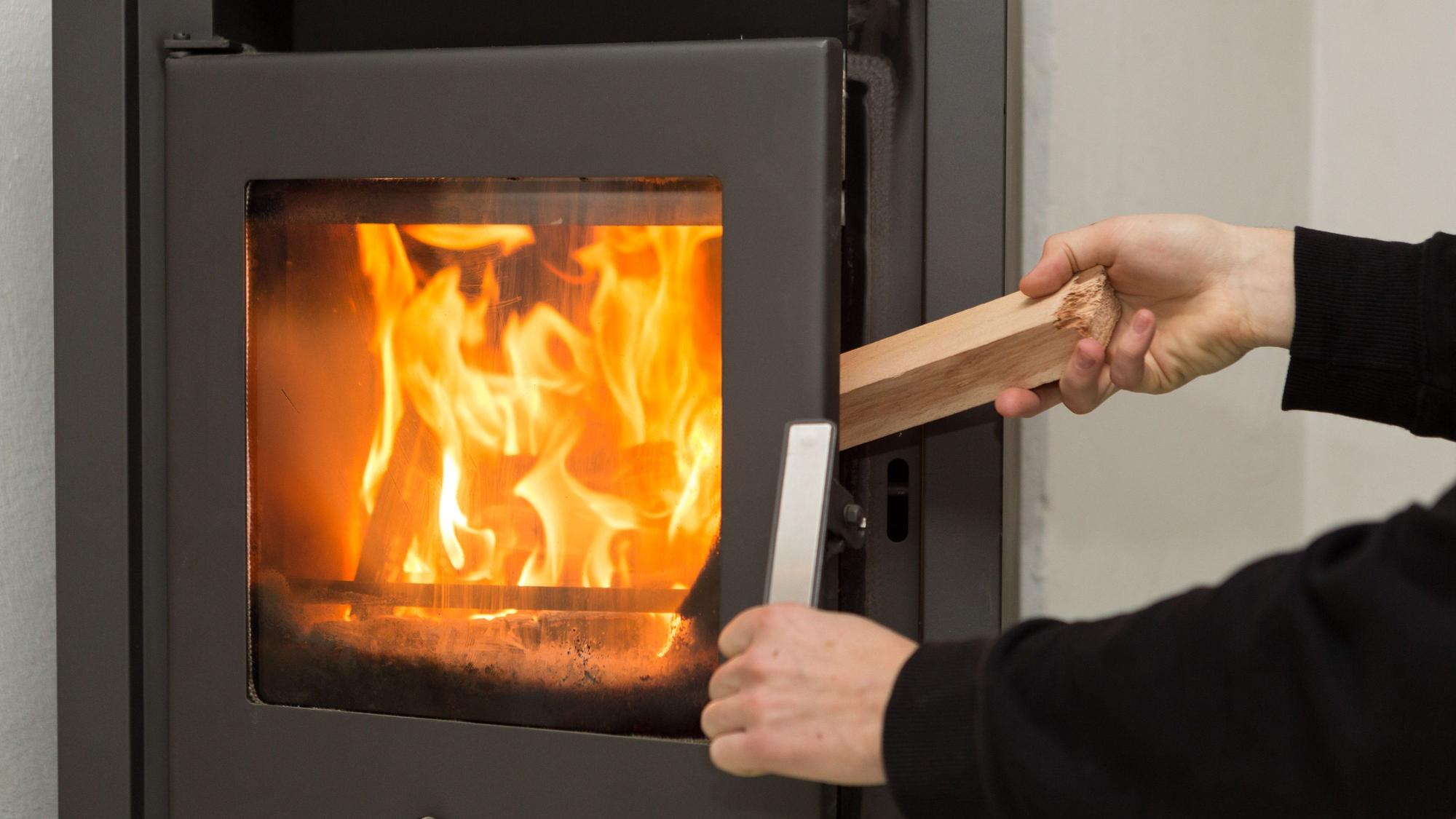 Eine Person legt ein Stück Holz in einen brennenden Kamin.