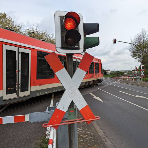 Ein Regionalexpress überquert einen Bahnübergang hinter geschlossenen Schranken.