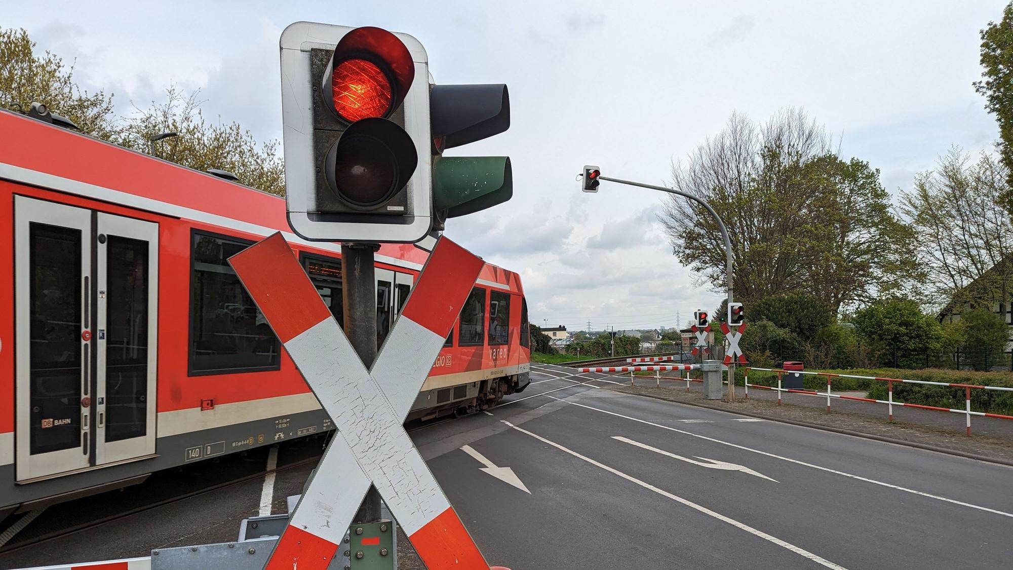 Ein Zug passiert einen Bahnübergang mit rotem Signal und heruntergelassenen Schranken.