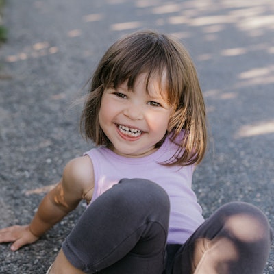 Ein kleines Mädchen sitzt auf dem Boden und lacht.