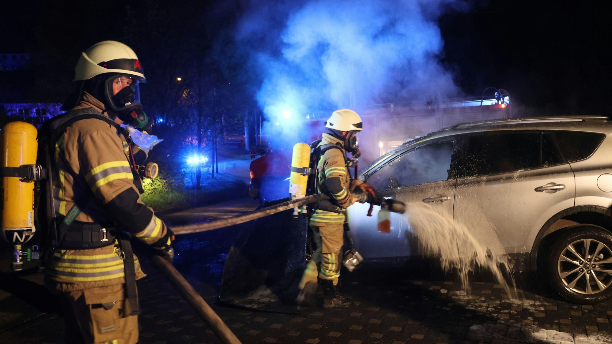 Zwei Feuerwehrmänner löschen ein qualmendes Auto.
