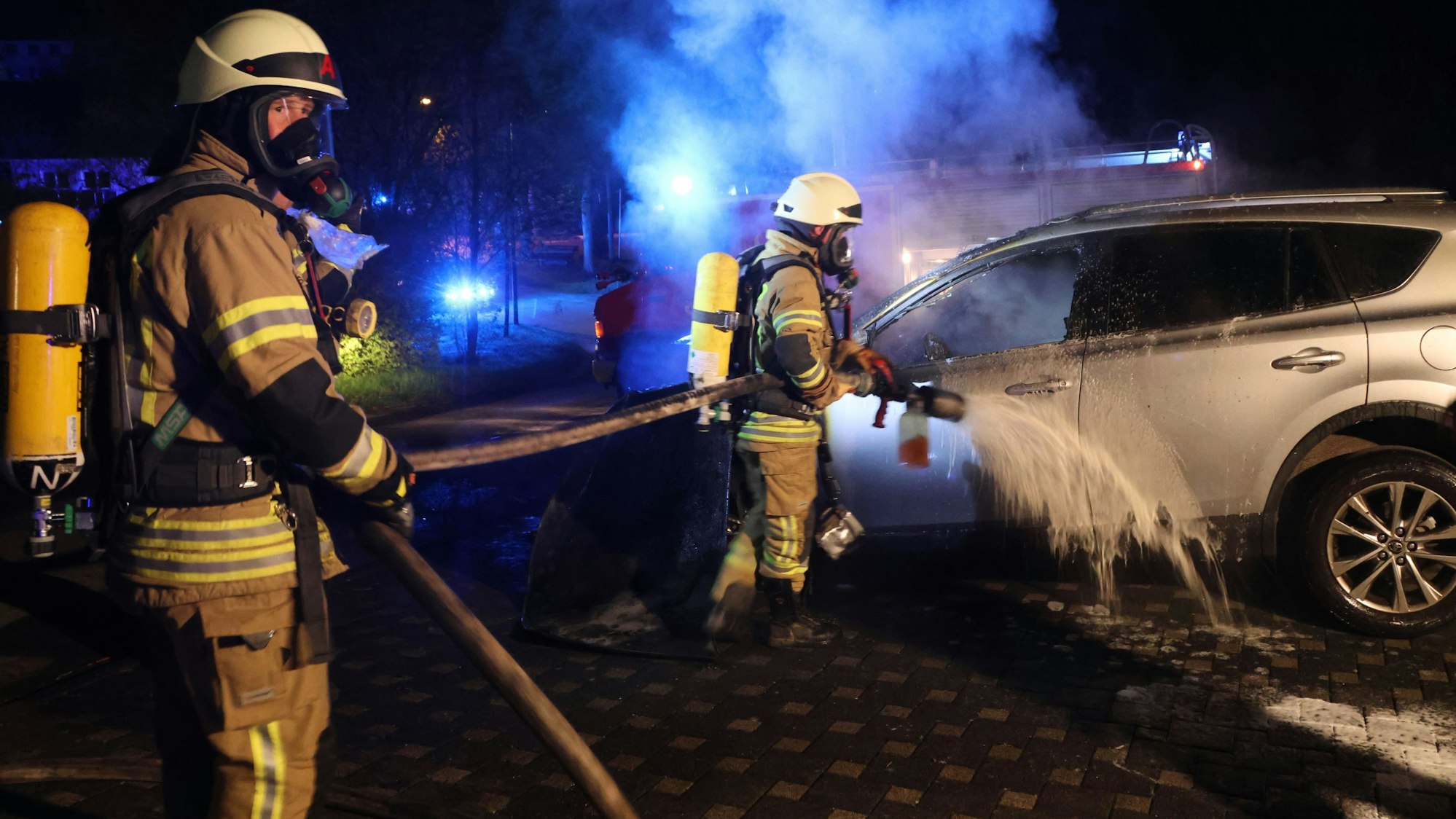 Zwei Feuerwehrmänner löschen ein qualmendes Auto.