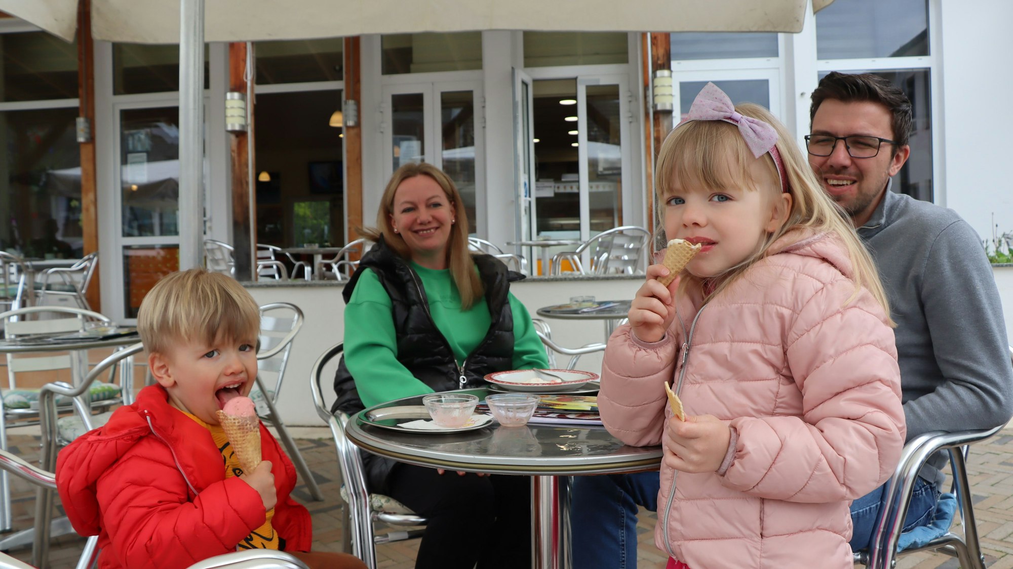 Zwei kleine Kinder essen Eis an einem Tisch vor einem Eiscafé