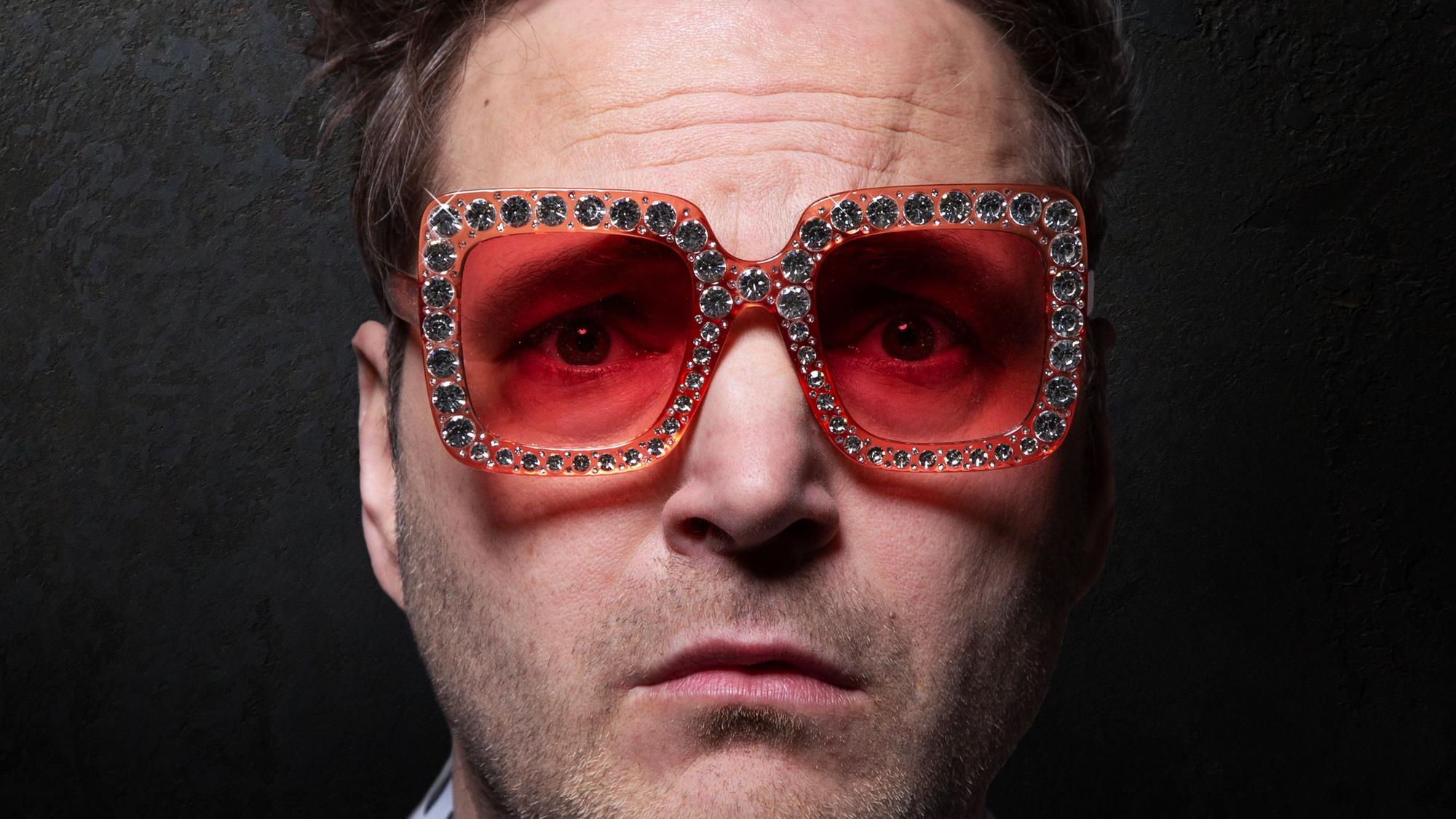 Paul Panzer trägt eine pink, glitzernde Sonnenbrille und schaut besorgt in die Kamera.