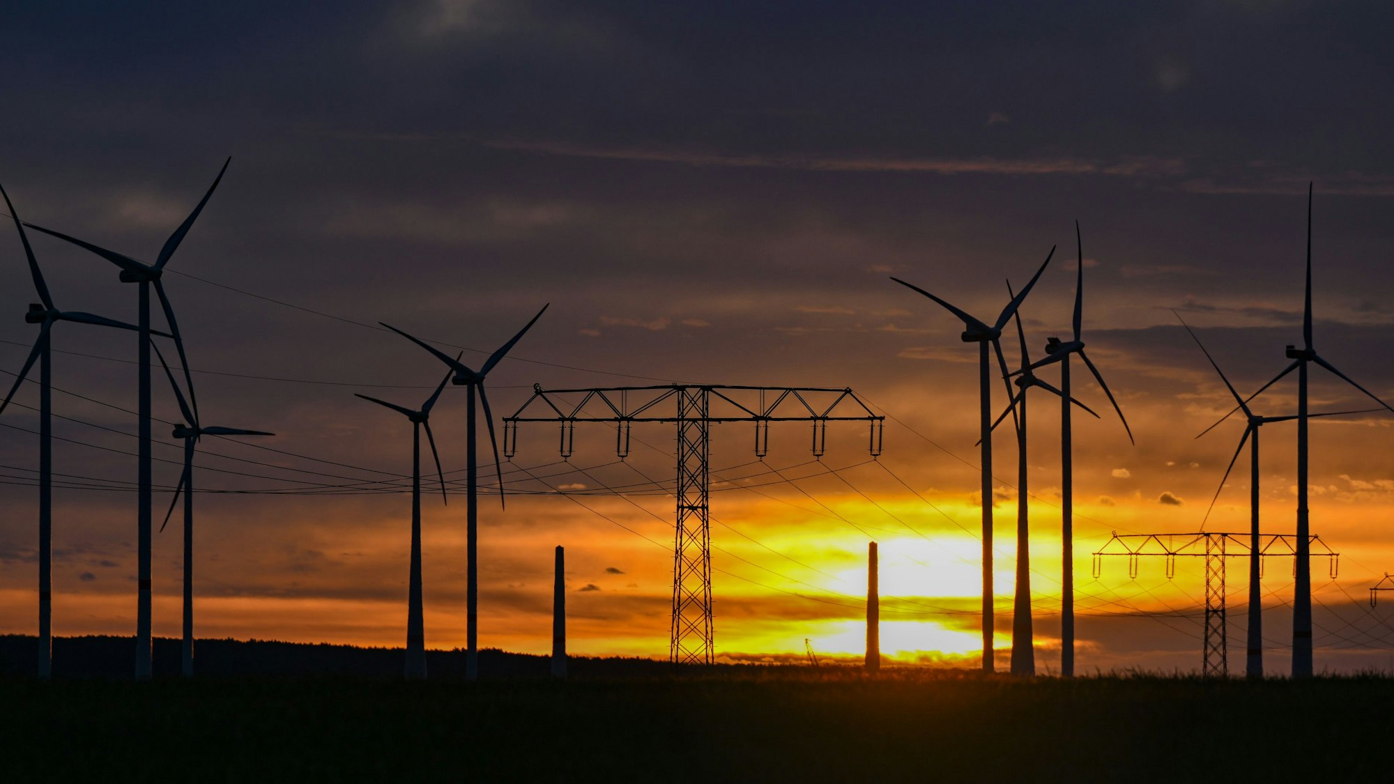 Landschaft mit Windrädern und Strommasten.
