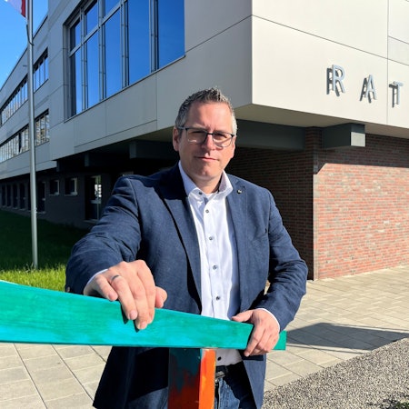 Ein Mann mit Brille steht an einem Geländer vor einem Rathaus.