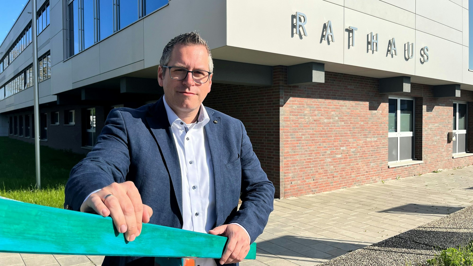 Ein Mann mit Brille steht an einem Geländer vor einem Rathaus.