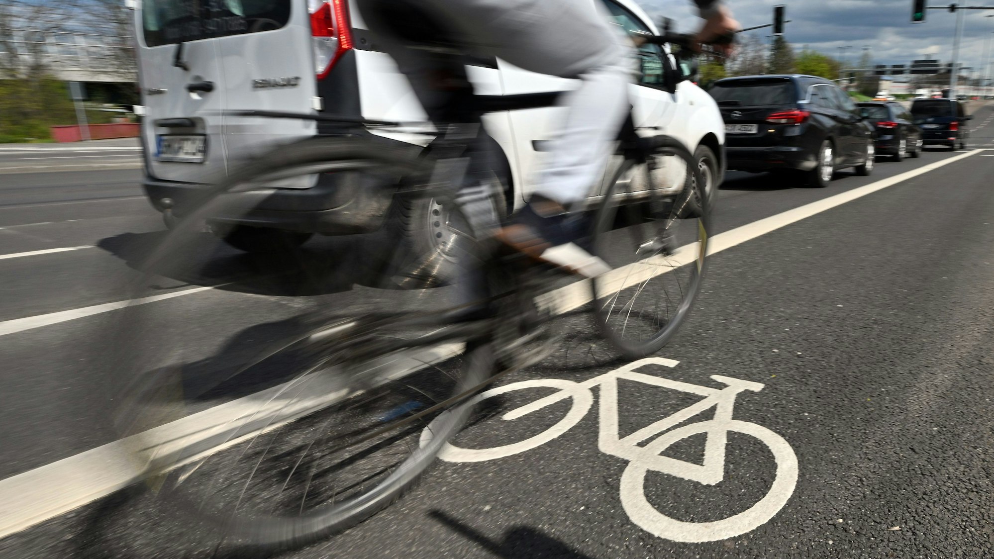 Ein Fahrradfahrer ist auf dem Radweg einer viel befahrenen Straße unterwegs.