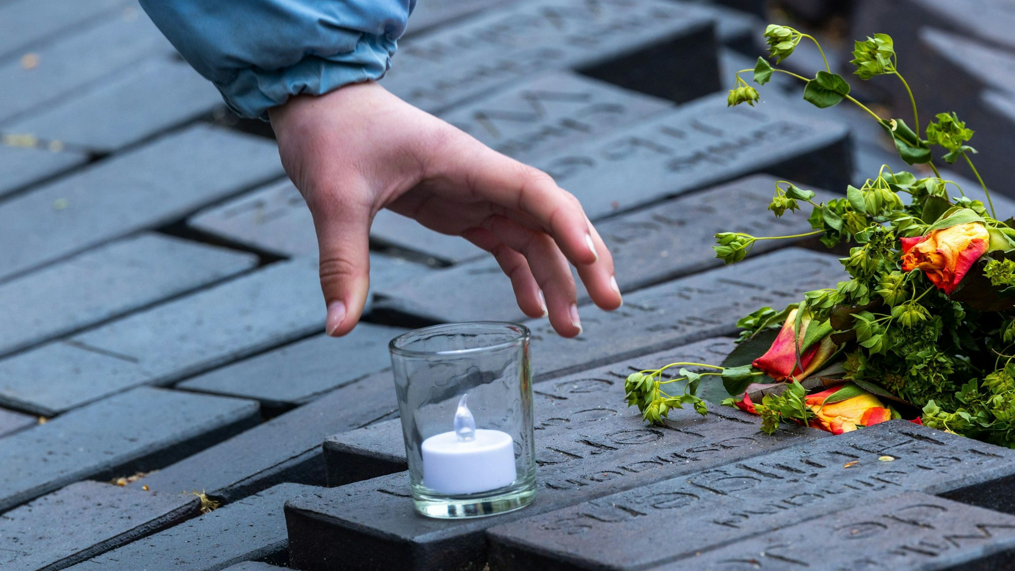 Angehörige und Gäste der Gedenkfeier stellen Kerzen auf die Steinreihen mit Namen von ehemaligen Häftlingen der KZ-Wöbbelin-Außenstelle.