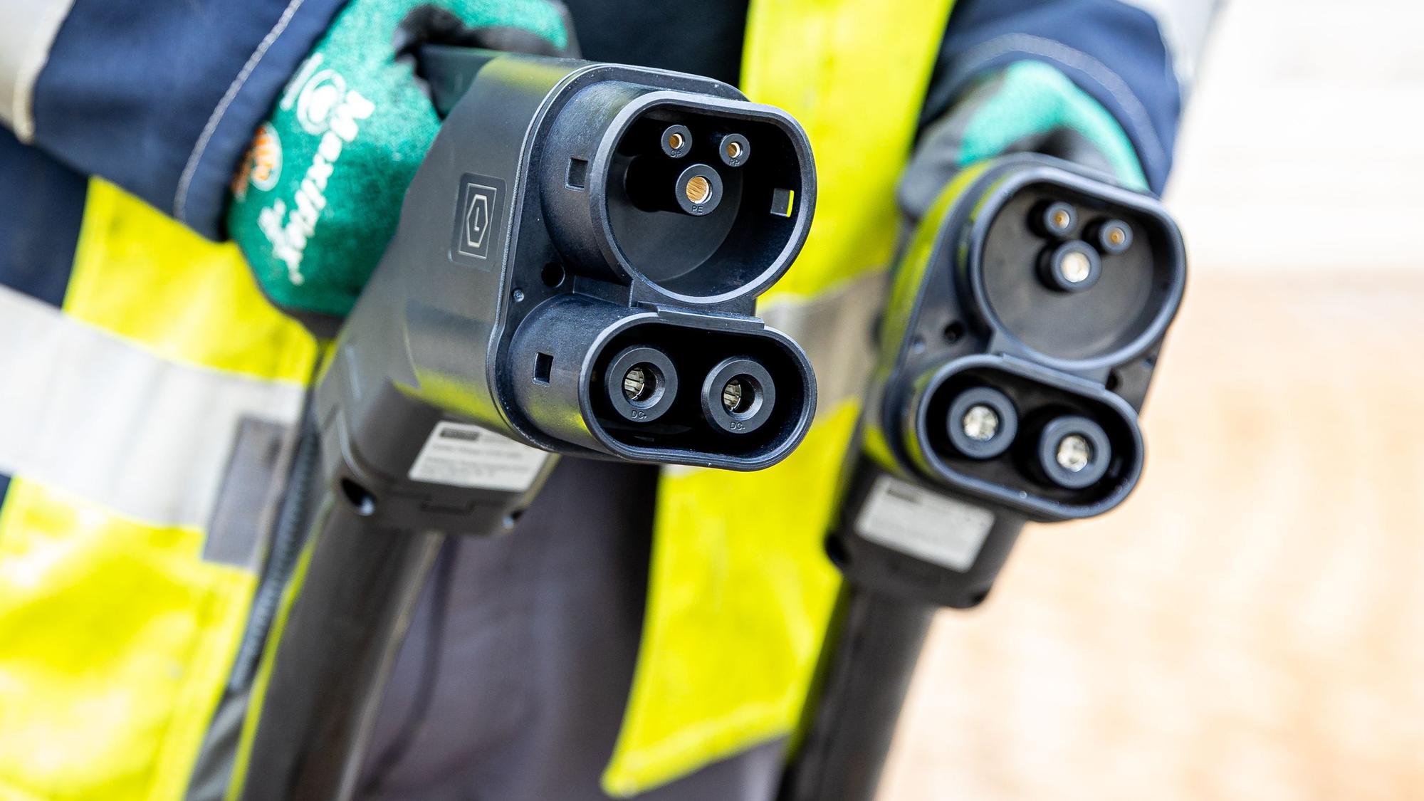 Ein Techniker hält nach der Installation einer Ladesäule für Elektroautos zwei Ladekabel in seinen Händen.