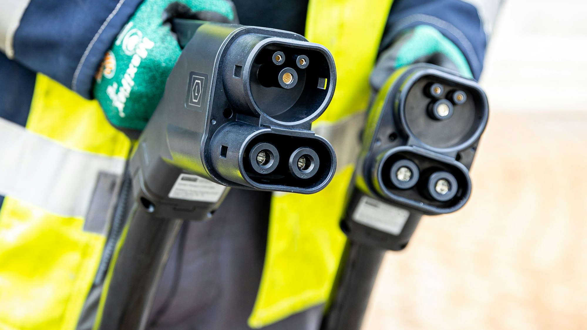 Ein Techniker hält nach der Installation einer Ladesäule für Elektroautos zwei Ladekabel in seinen Händen.