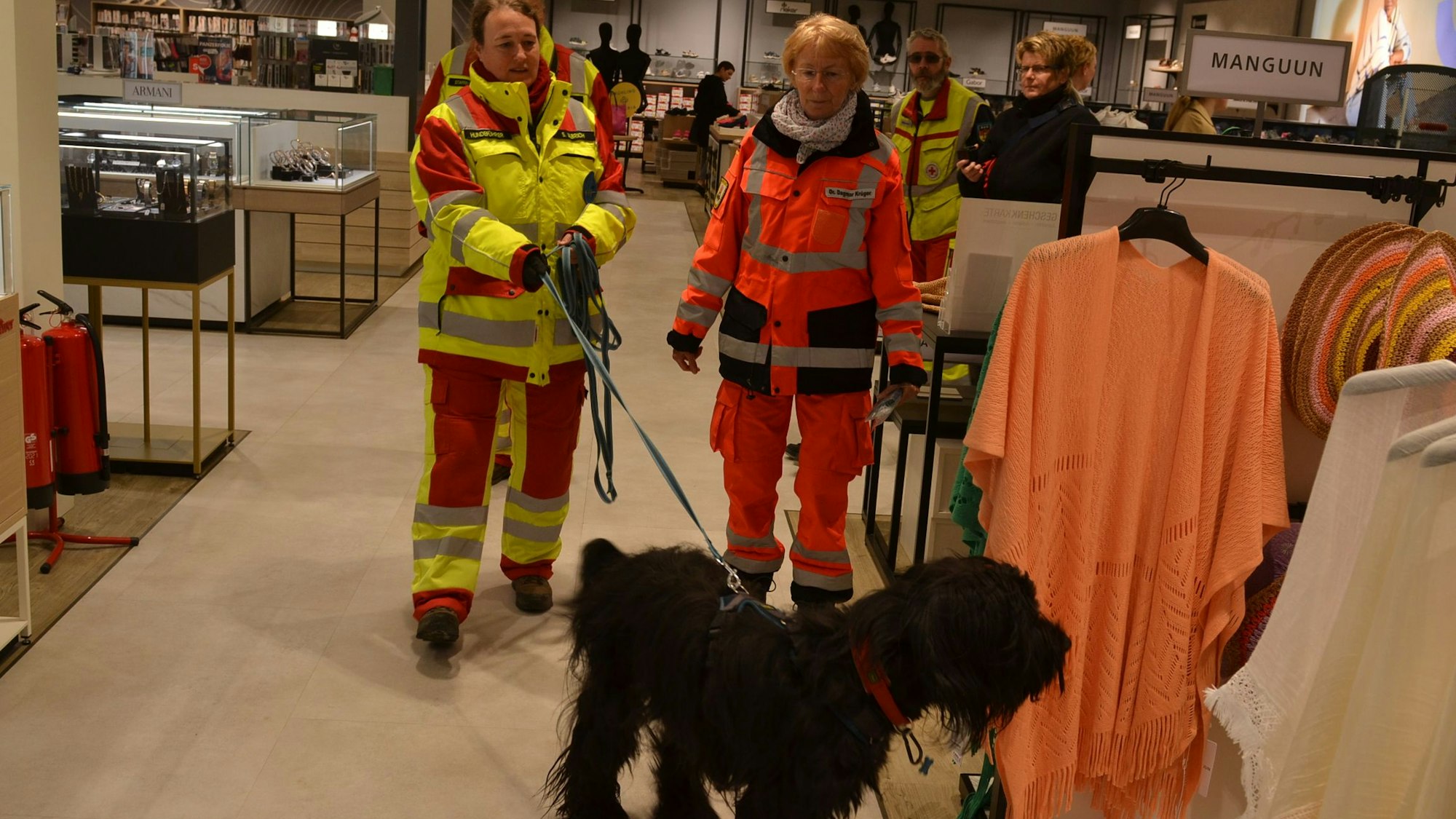 Zwei Frauen in Einsatzkleidung und ein Rettungshund trainieren in einem Kaufhaus die Suche nach Vermissten.