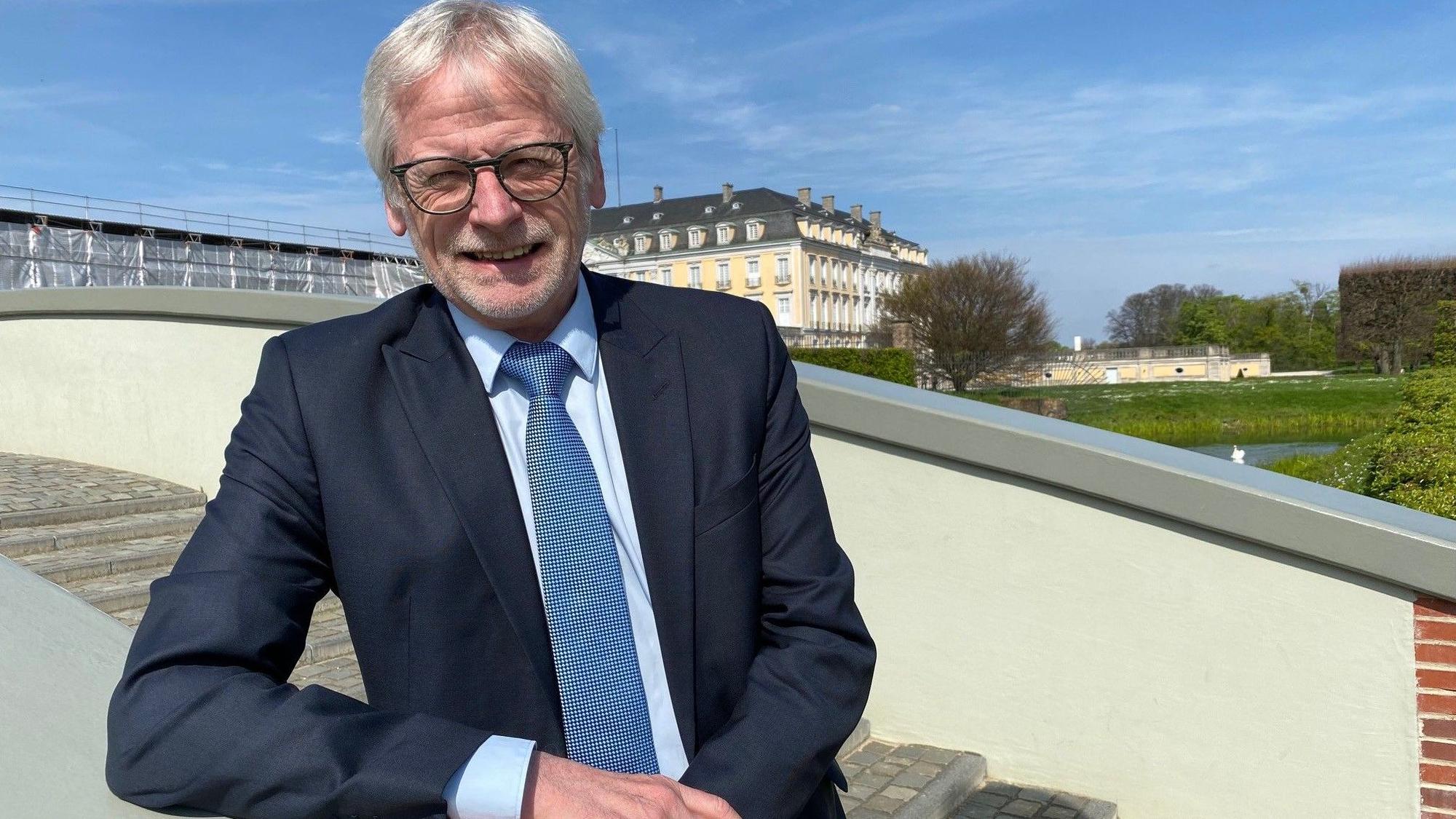 Der Bürgermeister steht in einem blauen Anzug auf einer Treppe und blickt lächelnd in die Kamera.