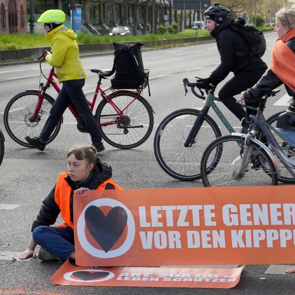 Cyclists drive unhindered past climate activists who have their hands glued to the ground during a climate protest in Berlin, Germany, Thursday, April 27, 2023. Activists of the 'Letzte Generation' (Last Generation) blocked streets in Berlin on Thursday to protest against the climate policy of the German government. (AP Photo/Michael Sohn)