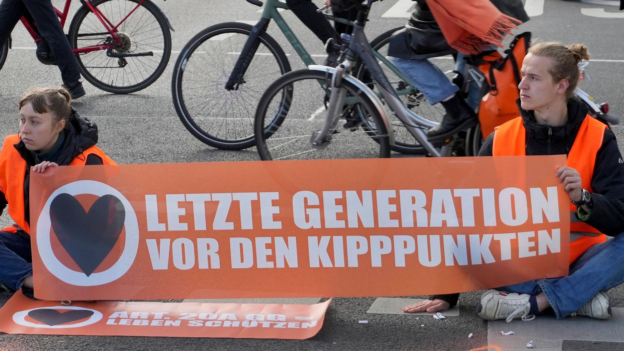 Cyclists drive unhindered past climate activists who have their hands glued to the ground during a climate protest in Berlin, Germany, Thursday, April 27, 2023. Activists of the 'Letzte Generation' (Last Generation) blocked streets in Berlin on Thursday to protest against the climate policy of the German government. (AP Photo/Michael Sohn)