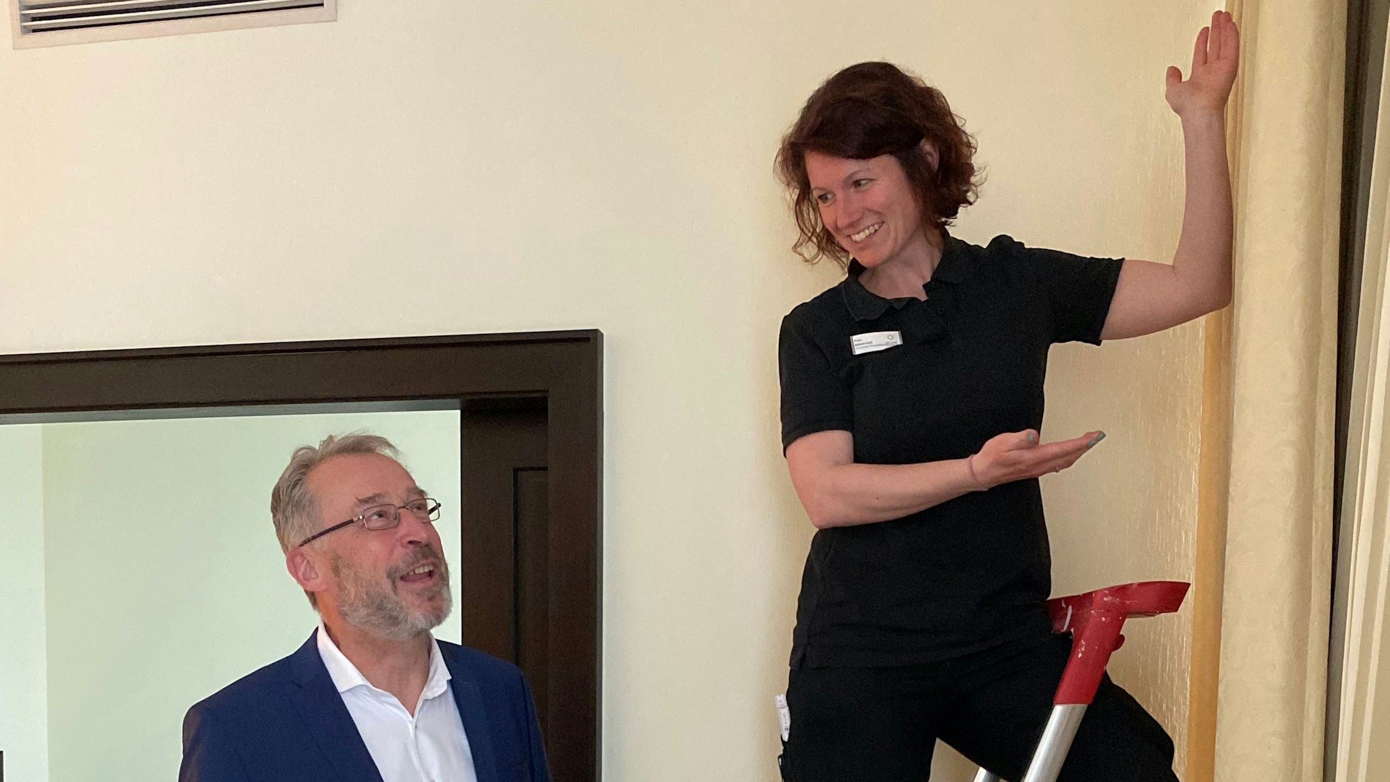 Eine Frau stehjt auf einer Leiter, ein Mann schaut ihr zu.