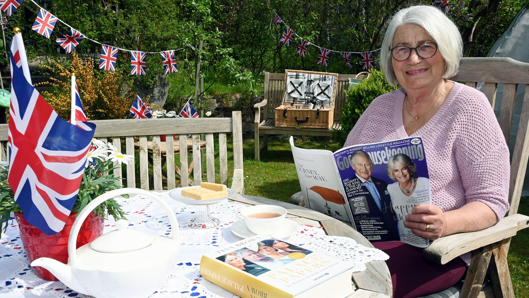 Eine Frau mit kinnlangen grauen Haaren sitzt in einem mit britischen Flaggen festlich geschmückten Garten.